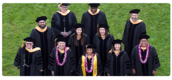 第一批毕业的DSW学生戴着帽子、长袍和兜帽对着镜头微笑